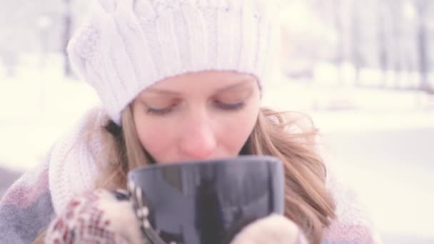 Mooie blonde in een witte gebreide muts in een winter park. Ze drinkt iets warm. Koesteren — Stockvideo