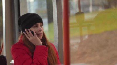 Genç kadın cep telefonu üzerinde otobüs yolculuğu akşam sırasında konuşurken. Ufuk kentsel trafik otobüs pencere yavaş 4k vurdu