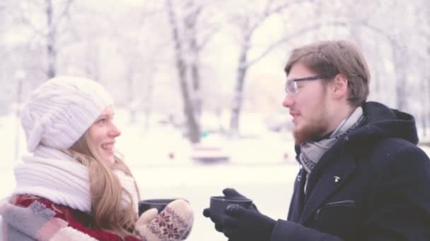 Jongeman en meisje praten in de winter in een besneeuwde park, warme koffie drinken — Stockvideo