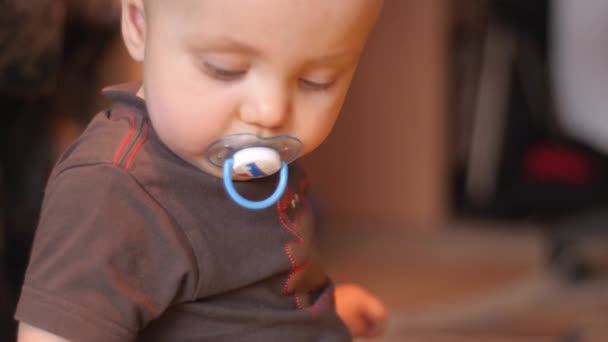 Niño con un chupete en la boca sentado en el suelo y tocando curiosamente la lente de una vieja cámara. Imágenes de vista lateral interior 4K . — Vídeos de Stock