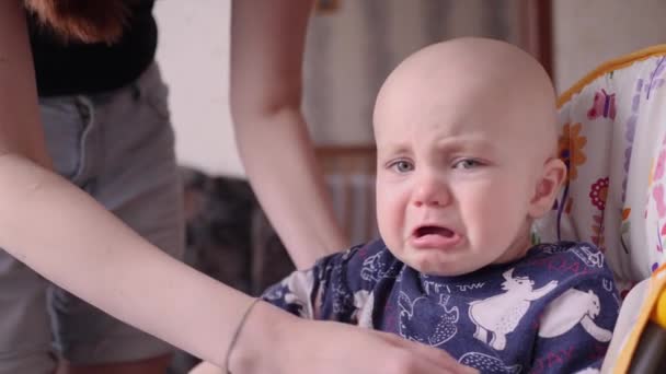 Mamá toma en sus brazos a un bebé llorando que se sienta en una silla para alimentarse — Vídeos de Stock