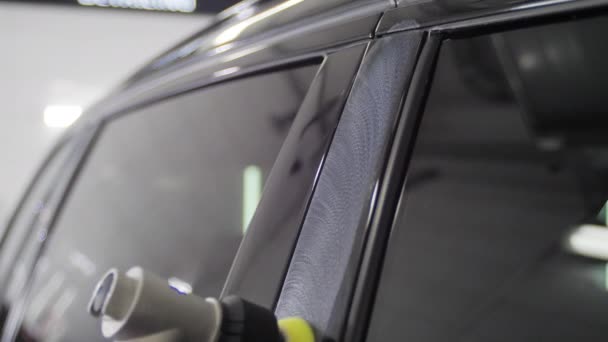 Рабочий полирует двери черной машины специальным устройством в автомойке. 4K замедленная съемка крупным планом . — стоковое видео