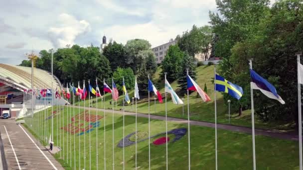 Vuelo sobre un gran número de banderas en una fila ondeando en el viento en el parque de la ciudad durante un festival internacional de arte con un escenario en la distancia en el fondo. Drone aéreo filmado en video 4K . — Vídeo de stock