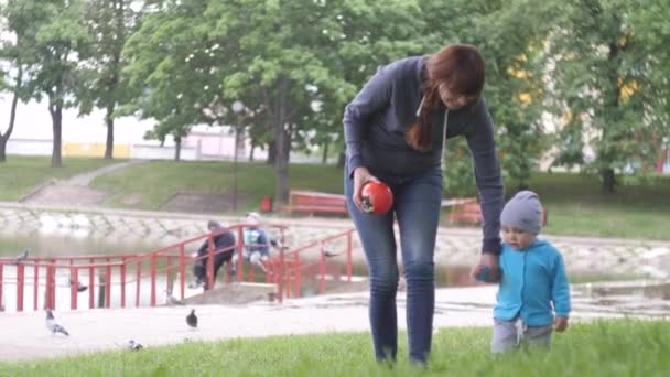 Junge Frau mit ihrem kleinen Sohn spazieren im Stadtpark an einem bewölkten Sommertag mit Teich und Bäumen im Hintergrund in 4k Zeitlupenvideo. — Stockvideo