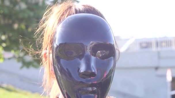 Ritratto di una giovane bruna carismatica che nasconde il suo volto dietro la maschera nera di un'installazione d'arte e poi lo abbassa sullo sfondo della città — Video Stock