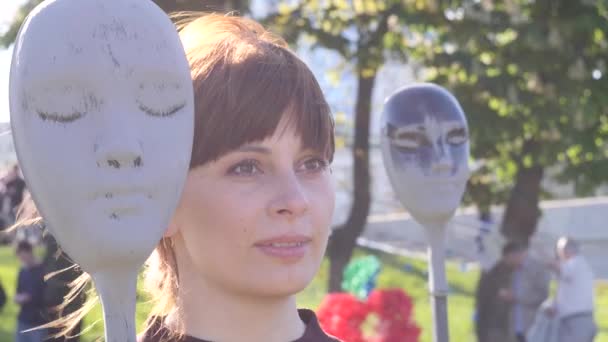 Porträt einer jungen schönen brünetten Frau, die in der Nähe der Maske einer Kunstinstallation vor dem Hintergrund der Stadt für die Kamera posiert, Nahaufnahme Video in Zeitlupe in 4k — Stockvideo