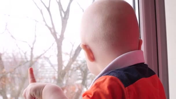 El niño se regocija sonriendo. Dibuja una mano en la ventana. A cámara lenta. Feliz bebé mira por la ventana . — Vídeo de stock