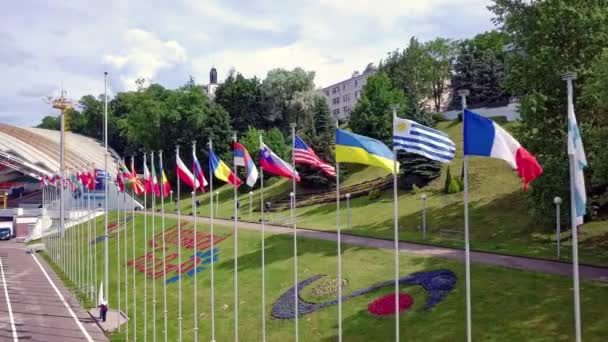 Drone flies past over a large number of country flags in a row fluttering in the wind during an festival of nations and moves to the amphitheater on the background. Aerial shot in 4K video. — Stock Video