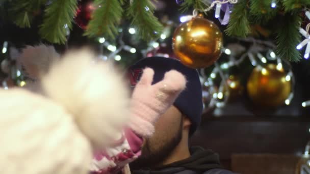 Homem pai barbudo e sua filha bebê estão brincando com bolas de Natal e luzes de fadas na decoração na rua da cidade noturna. Natal e ano novo conceito de férias em vídeo em câmera lenta 4K . — Vídeo de Stock