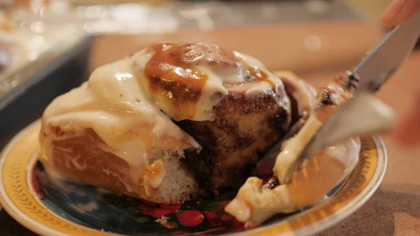 Femme ou homme mains coupe un pain à la cannelle chaud frais tartiné avec une crème blanche crémeuse-caramel sur la belle plaque au ralenti vidéo 4K . — Photo