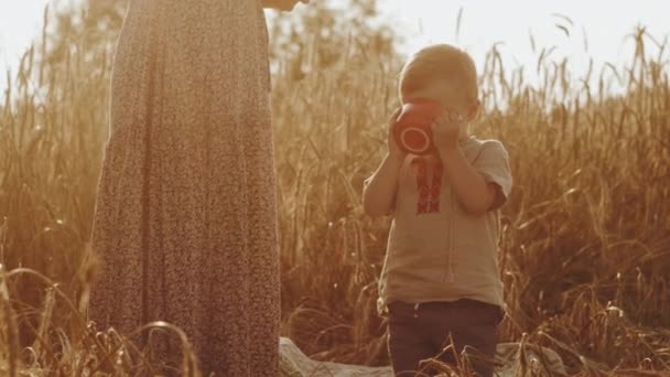 A lovely little boy is drinking from a mug. Mom with a baby in national costumes at a picnic on a rye field . 3d rendering. The concept of a happy family and family values — 비디오