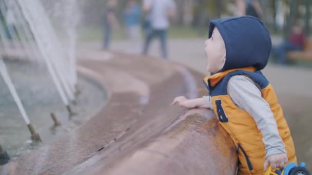 A kölyök a szökőkútnál játszik. Gyermek öröm, boldog gyermekkor. Családi értékek — Stock videók