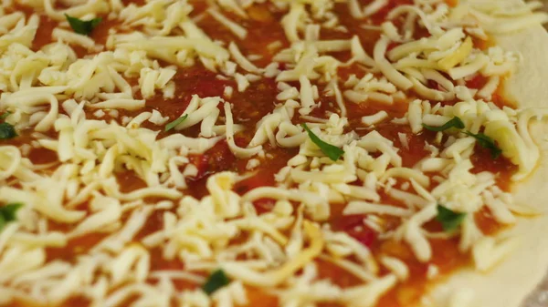 Cozinhar pizza. Chef colocar queijo e manjericão na base da pizza untada com pasta de tomate. Um homem ou mulher está envolvido em negócios em casa preparando uma deliciosa pizza — Fotografia de Stock