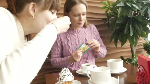 Két csinos nő barátok beszélgetnek hírek, kávézás és eszik fagylaltot kávészünetben kávézóban dekoratív fa és nagy ablak a háttérben. Közelkép portré nézet forgatott 4k videó. — Stock videók
