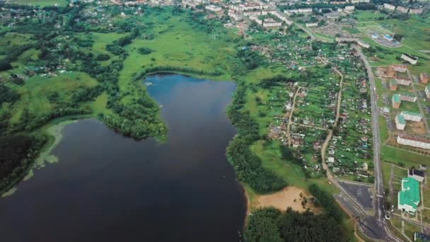 Pássaros panorâmicos vista de olhos com câmera rotativa de um voo de drone sobre uma cidade em pé em um lago e uma floresta na margem oposta em um dia de verão. Fotografia de conceito de paisagem aérea em vídeo 4K . — Vídeo de Stock