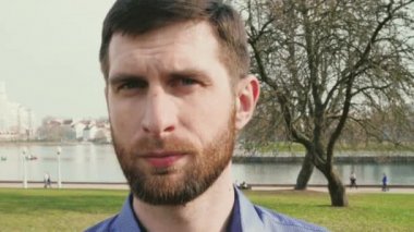 kameraya bakarak dondurulmuş ve sonra yaz şehir arka plan yavaş hareket üzerinde gülümseyen bir sakallı genç adam portre 4k video yakın