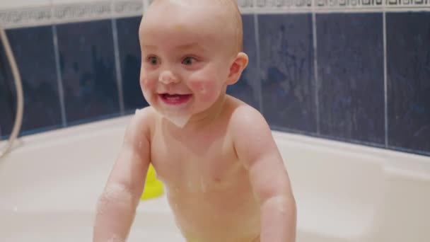 Pequeño bebé con jabón suds en su cara de pie en el baño y divertirse y sonreír a su madre detrás de la cámara por lo que luego el niño alcanzar el estante en cámara lenta de tamaño medio 4K metraje — Vídeos de Stock