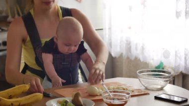 Küçük bir çocukla oturan genç bir kadın mutfak masasında otururken yumurta kesiyor ve bitirdikten sonra çocuğunu öpüyor. Anne ev işleri konsepti. 4k videosunda yavaş çekim ön görünümü