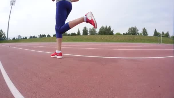 Una joven atleta en francotiradores rojos corriendo frente a la cámara durante un día de entrenamiento en el estadio de atletismo de la ciudad en cámara 4K en cámara UHD — Vídeos de Stock