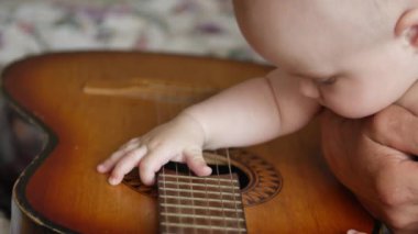 Küçük bebek klasik akustik gitar tellerine dokunup çekiyor. Bebekler ve yeni yürümeye başlayanlar konsepti. 4k video 'da ön görünüm yakın çekim.