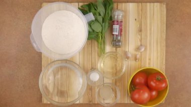 Şefin kadınları, ahşap tepsiden peynirli pepperonili pizza hazırlamak için gereken tüm malzemeleri sırayla kaldırır. Üst görünüm hızlandırılmış 4k video.