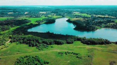 İHA, güneşli yaz günlerinde bulutun gölgesinin arka planda yüzdüğü göle doğru uçar. 4k video içerisindeki hava görüntüsü yavaş çekim.