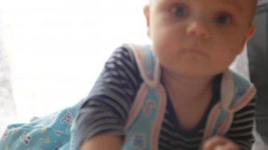 Küçük çocuk kameraya bakıyor, karnının üstünde emeklemeye ve eliyle yakalamaya çalışıyor. Yavaş çekim ön görünüm 4k portresi kapat.