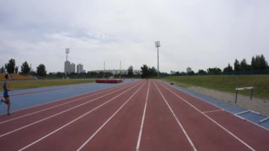 Genç bir sporcu, Uhd 'un geniş mercek kamerasında ağır çekim 4K video eğitimi sırasında şehir spor stadyumunda koşuyor.