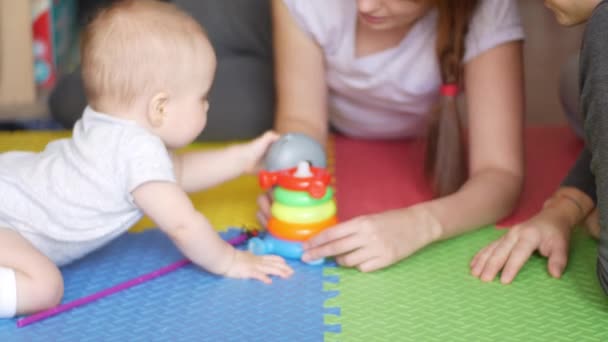 Donna, uomo e il loro bambino stanno giocando sul pavimento su un tappeto colorato e i genitori stanno insegnando al figlio a assemblare una piramide giocattolo. Famiglia e insegnamento concetto di bambini. Vista frontale medio girato in video 4K . — Video Stock