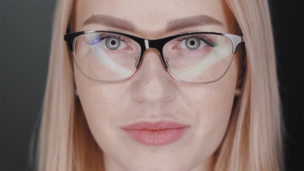 Femme aux cheveux blonds dans des lunettes regarde avec confiance la caméra, puis sourit large pour montrer ses orthèses dentaires debout sur fond noir. Concept de traitement orthodontique. Slowmotion portrait vidéo en 4K — Video