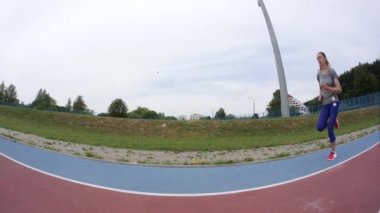 A young beautiful sport woman jogging past the camera at the city stadium on a running training in slow motion close up 4K video on UHD wide lens camera