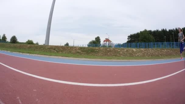 A young beautiful woman jogger running past the camera during a day running training at the city stadium in slow motion 4K video on UHD wide lens camera — Αρχείο Βίντεο