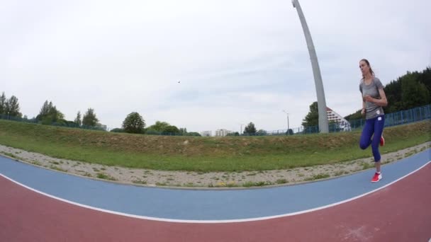 Una joven mujer hermosa deporte trotando más allá de la cámara en el estadio de la ciudad en un entrenamiento de carrera en cámara lenta de cerca de vídeo 4K en la cámara de lente ancha UHD — Vídeos de Stock