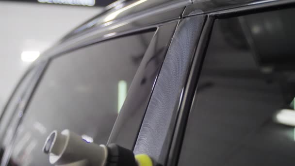 Worker man is polishing a black car doors with a special device in a car washing station. 4K slow motion close up shot video. — Stock Video