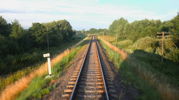 Vista trasera del ferrocarril y una hermosa naturaleza verde desde un tren que pasa por tierras rurales. Concepto de viaje ferroviario o turismo ferroviario. Vista trasera en cámara lenta 4K video . — Foto de Stock