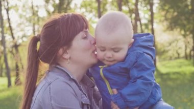 Küçük çocuğu olan boğucu bir anne parkta yürüyor. Annem bebeği öpüyor. Gün batımında yürüyen çocuk parktaki çimlerin üzerinde yatıyor. Aile yürüyüşleri. Anneler umursar
