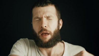 Sakallı, dirseğinden hapşıran yakışıklı bir adam. Sakallı adam siyah arka planda gözleri kapalı hapşırıyor. Alerjik hapşırma ya da hapşırma hastalık belirtisi. Ağır çekim 4K videosunu kapat.