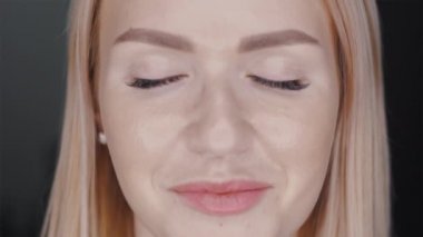 Genç kadın, siyah arka planda gözlerini aç. Stüdyoda kameraya bakan gülümseyen kıza yaklaş. Gülümseyen sarışın bir model. Kadın doğası güzelliği