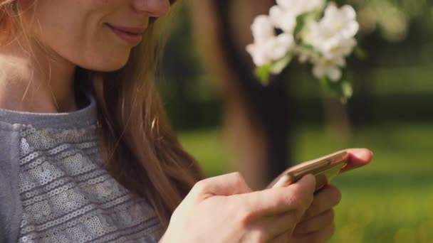 Ένα νεαρό κορίτσι στο πάρκο γράφει ένα μήνυμα στο τηλέφωνο. — Αρχείο Βίντεο