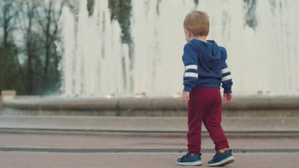 En liten pojke går vid fontänen. Gå med dina föräldrar. Föräldravård. Helg i parken — Stockvideo