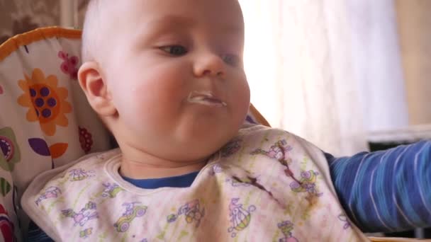 Voeden baby met een lepel door de moeders hand, terwijl kleine schattige jongen kijkt rond 4K slow mo close-up — Stockvideo