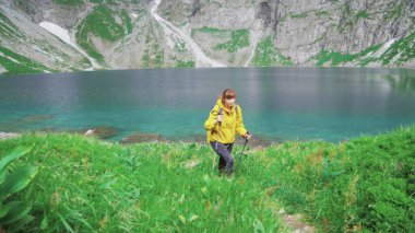 Genç bir turist kadın güzel bir dağ gölünün tepesinde kuzeye doğru yürüyor ve macerasının tadını çıkarıyor. Spor eğlencesi aktivitesi. Yaz tatili turizmi. Yavaş çekim 4K video.