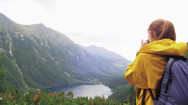 Une touriste fait une photo d'un beau lac de montagne et de sommets verts devant elle, puis elle se retourne et tire des montagnes derrière la caméra. Concept de voyage ralenti 4K vidéo . — Video