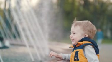 Küçük bir çocuk fıskiyede oynar ve sevinir. Çocuklar neşe, çocuklar kahkaha