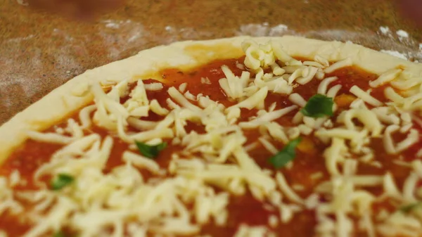 Pizza kochen. Chef legt Käse und Basilikum auf den Boden der mit Tomatenmark eingefetteten Pizza. Ein Mann oder eine Frau ist mit der Zubereitung einer leckeren Pizza beschäftigt — Stockfoto