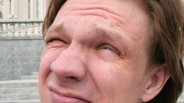 portrait of a white charismatic man looking at the sun and camera on city architecture background and squinting laughing slow motion close up video in 4K