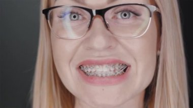 Çekici, neşeli, diş teli takan, harika zaman geçiren, eğlenen, gülümseyen, mutluluk ve neşe saçan, siyah arka planda duran sarışın kadın.