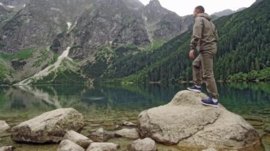 Turistler dağ kıyısındaki bir kayaya tırmanıp manzaranın fotoğraflarını çekerler. Seyahat ve macera kavramı. Yavaş çekim