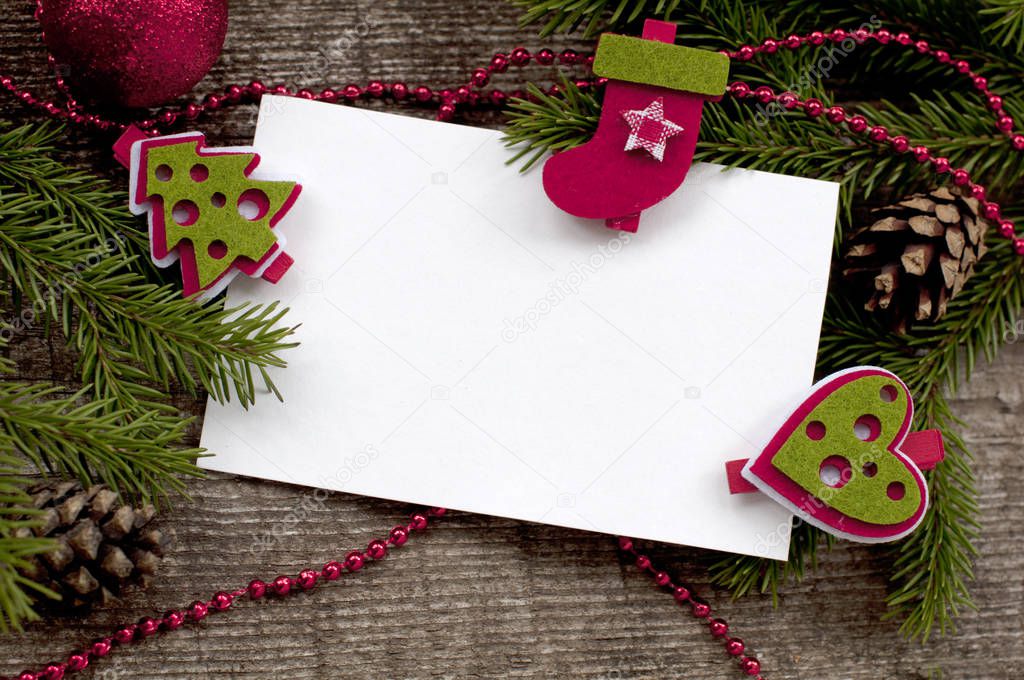 Christmas card with clean sheets the attached decorative clothespegs to fir-tree branches and white paper on a wooden background. 