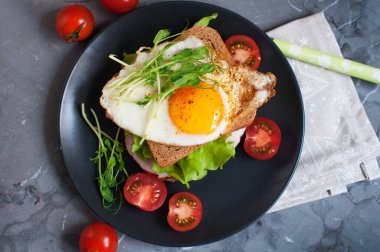 Kızarmış yumurtalı sandviç, et, domates, bezelye filizi ve salata. Siyah bir tabakta kahvaltı. Üst görünüm